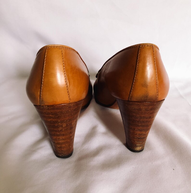 May include: A pair of vintage brown leather heels with wooden cone-shaped heels. The shoes have a classic design with a rounded toe and a small decorative detail on the vamp. The heels appear to be approximately 7.6 cm tall.