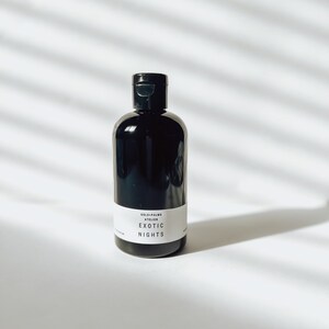 May include: A black bottle with a white label that reads "GOLD PALMS ATELIER EXOTIC NIGHTS".