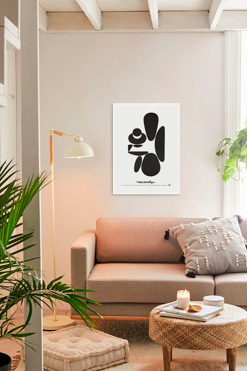 May include: Black and white abstract art print with the word "Vacarely" in cursive at the bottom. The print is framed and hanging on a white wall above a light brown couch.
