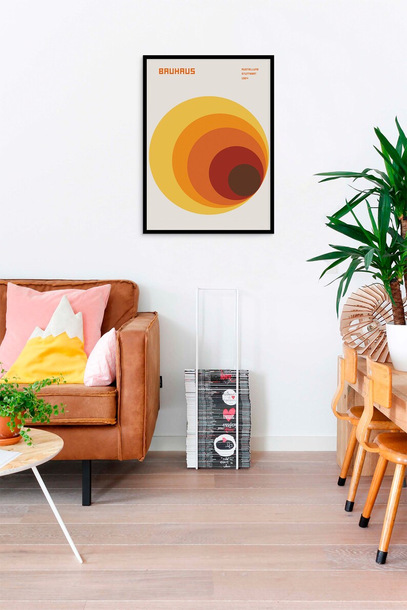 May include: A framed print with a Bauhaus design featuring a series of concentric circles in shades of orange, yellow, and brown. The print has the text "BAUHHAUS" and "INSTITUT F&Uuml;R GESTALTUNG" in black.