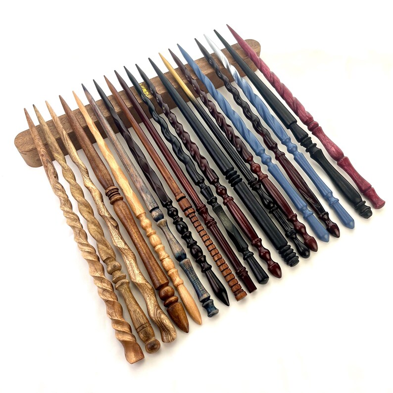 Puede incluir: Una colecci&oacute;n de varitas de madera hechas a mano en varios colores y dise&ntilde;os. Las varitas se exhiben en un soporte de madera, mostrando una gama de estilos, desde torcidos hasta intrincadamente tallados. Los colores incluyen tonos de madera natural, negro, azul y rojo.