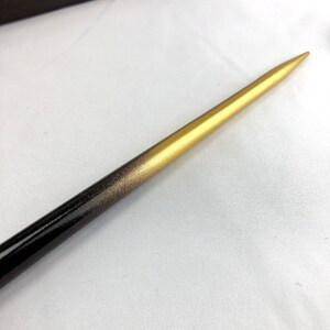 May include: A wooden hair stick with a gradient design. The stick transitions from a black base to a gold tip, with a speckled gold middle section. The pointed end is gold, and the stick is smooth and polished.