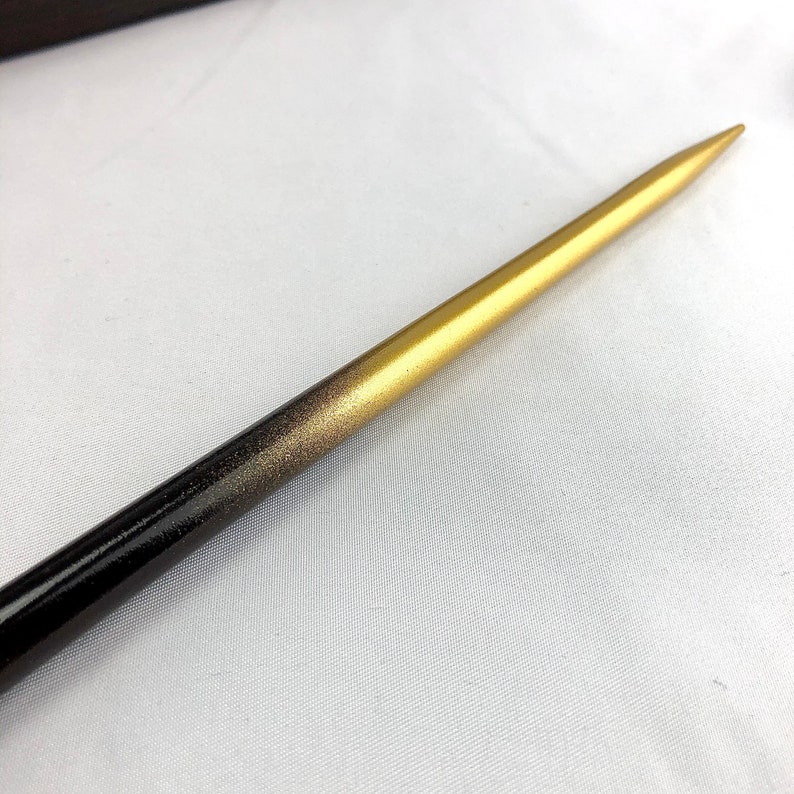 May include: A wooden hair stick with a gradient design. The stick transitions from a black base to a gold tip, with a speckled gold middle section. The pointed end is gold, and the stick is smooth and polished.