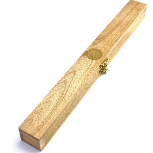 May include: A rectangular wooden box with a light brown finish. The box has a gold-colored clasp and a circular gold emblem on the lid. The box is made of wood and has a natural grain pattern.