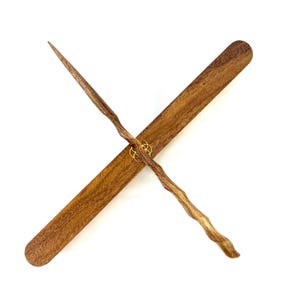 May include: Two wooden wands crossed over a wooden rectangular base. The wands are brown with a textured, naturalistic design, and are joined by a gold-colored ring. The base is a darker brown with a smooth, rectangular shape.