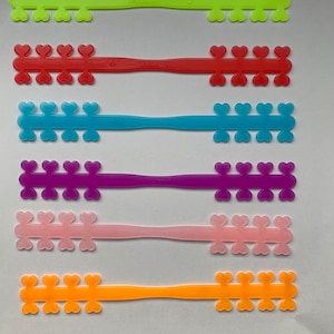 Puede incluir: Seis salvaorejas de plástico de colores con bucles en forma de corazón. Los salvaorejas son de los siguientes colores: verde, rojo, azul, morado, rosa y naranja.