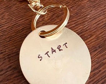 May include: A gold-colored key chain with a round tag that says "START" in brown lettering.