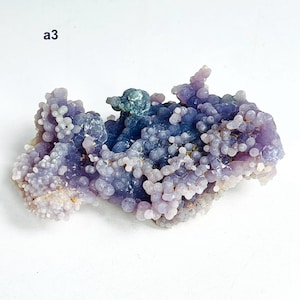 May include: A grape agate gemstone, displaying a distinctive botryoidal formation. The stone's colours range from purple and lavender to blue, with a crystalline texture. The text "a3" is visible in the upper left corner.