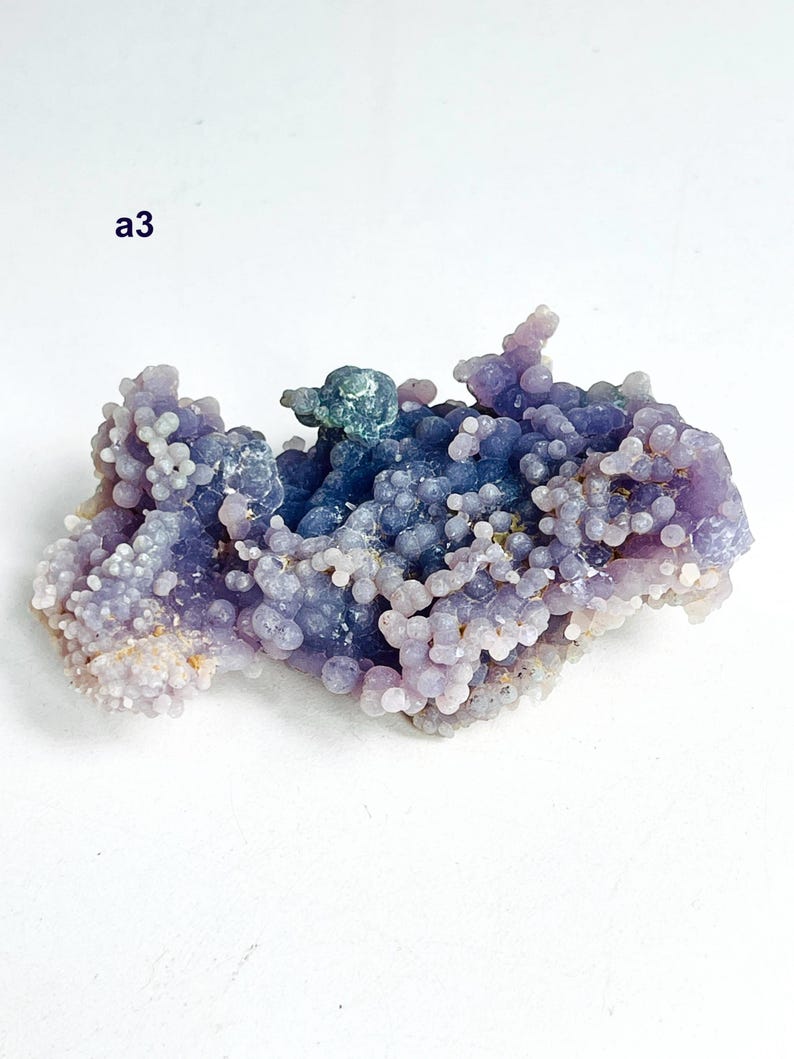 May include: A grape agate gemstone, displaying a distinctive botryoidal formation. The stone's colours range from purple and lavender to blue, with a crystalline texture. The text "a3" is visible in the upper left corner.