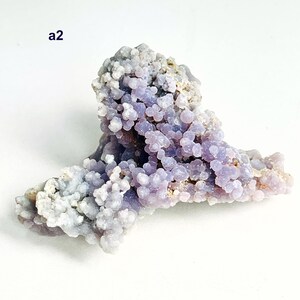May include: A grape agate mineral specimen with a distinctive botryoidal structure. The lavender-colored clusters are interspersed with areas of pale grey and white. The text "a2" is visible. This natural formation is a unique example of mineralogy.