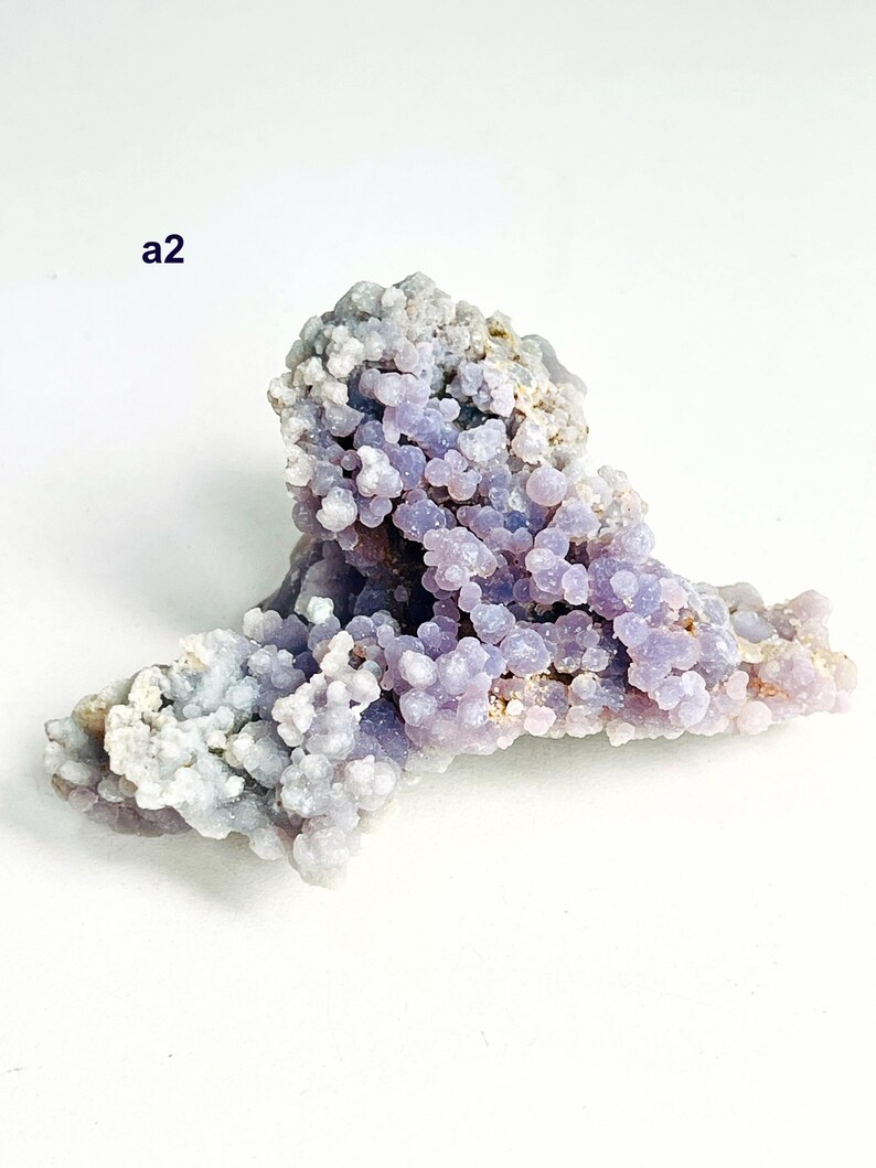 May include: A grape agate mineral specimen with a distinctive botryoidal structure. The lavender-colored clusters are interspersed with areas of pale grey and white. The text "a2" is visible. This natural formation is a unique example of mineralogy.