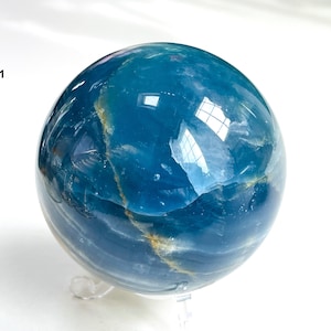 May include: A blue and white sphere of polished celestite, a type of mineral, on a clear stand. The sphere has a swirling pattern of blue and white.