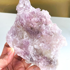 Könnte beinhalten: Ein großer, roher Amethyst-Kristallcluster. Der Kristall hat eine komplexe, stachelige Struktur und ist helllavendelfarben mit Bereichen von dunklerem Lila und Weiß. Die Textur ist rau und kristallin, mit einem natürlichen, unpolierten Aussehen.