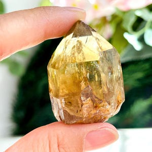 Könnte beinhalten: Eine goldene Citrin-Kristallspitze mit einer klaren, facettierten Form. Der Kristall hat ein natürliches, rohes Aussehen mit Einschlüssen und einem leichten Braunton.