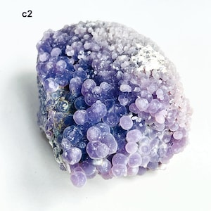 May include: A grape agate specimen, a mineral with a distinctive appearance. It features numerous small, spherical formations, resembling grapes, in varying shades of purple and lavender. The text "c2" is visible.
