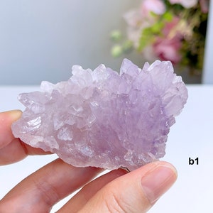 Könnte beinhalten: Ein Cluster aus Amethyst-Kristallen in Violett- und Lavendeltönen. Die Kristalle sind fächerförmig angeordnet und haben eine natürliche, raue Textur.