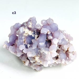 May include: A cluster of pale purple chalcedony crystals. The crystals have a bubbly, rounded form and a slightly translucent appearance. The text "c3" is visible in the upper left corner. The overall colour is a soft lavender with hints of white.