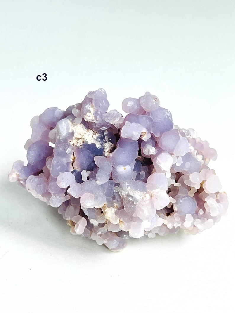 May include: A cluster of pale purple chalcedony crystals. The crystals have a bubbly, rounded form and a slightly translucent appearance. The text "c3" is visible in the upper left corner. The overall colour is a soft lavender with hints of white.