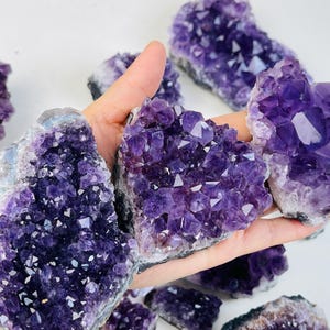 Könnte beinhalten: Eine Sammlung von Amethyst-Kristallgruppen in verschiedenen Größen und Formen. Die Kristalle sind tiefviolett und haben eine natürliche, raue Textur.