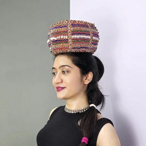 May include: A woman wearing a black crop top and black pants with a colorful beaded headpiece. She is wearing silver jewelry and has her hair pulled back in a ponytail.
