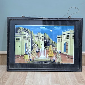 May include: A framed painting depicting a scene with people in a courtyard with a fountain in the center. The painting is done in a colorful style with a blue sky and white clouds. The frame is black and has a simple design.