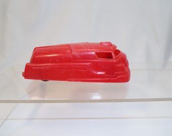 May include: A red plastic toy car with a rounded body and a single window. The car is sitting on a clear surface.