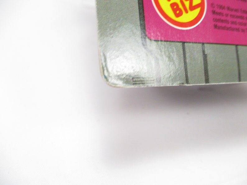 May include: Close-up of a product package corner. The package has a gray and pink color scheme with a yellow and red circular logo. Vertical gray lines are visible on the package. The text "BIZ" is visible in the logo.