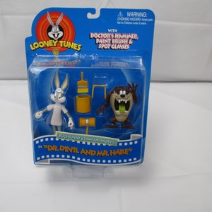 May include: A plastic package containing two action figures, Bugs Bunny and Taz, from the Looney Tunes cartoon. The package is blue and yellow and features the text "Looney Tunes" and "Dr. Devil and Mr. Hare".