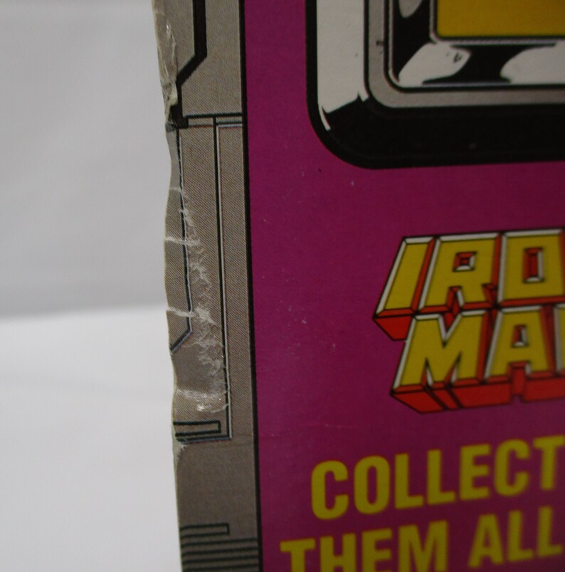 May include: A close-up of a pink and gray cardboard box with the words "Iron Man" in yellow and red letters. The text "Collect them all" is also visible in yellow letters.