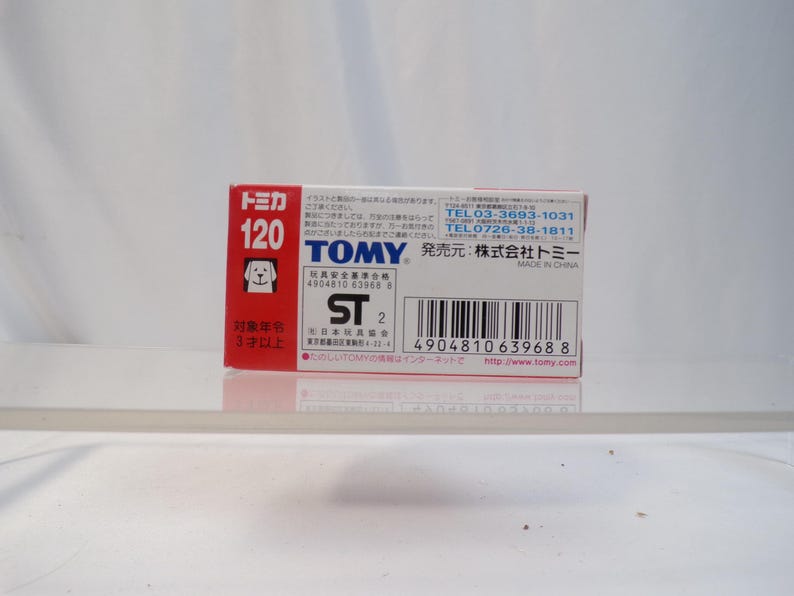May include: A small, rectangular box with Japanese text and graphics. The box is primarily red and white, with the number "120" prominently displayed. The brand name "TOMY" is visible, along with a barcode and other details.