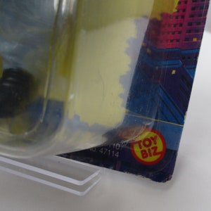 Pu&ograve; includere: Primo piano di una confezione di giocattoli in plastica con uno sfondo di citt&agrave; blu e viola. La confezione ha un logo "Toy Biz" rosso e giallo.