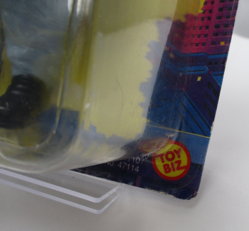 Pu&ograve; includere: Primo piano di una confezione di giocattoli in plastica con uno sfondo di citt&agrave; blu e viola. La confezione ha un logo "Toy Biz" rosso e giallo.