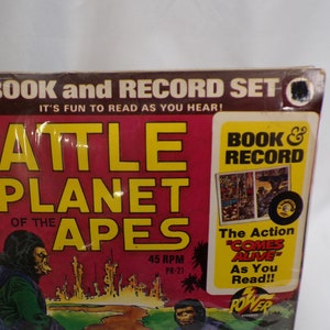 May include: A book and record set for "Battle for the Planet of the Apes". The cover features a red background with yellow text and a picture of a monkey in a green jacket. The record is black with a white label. The text on the cover reads "Book & Record" and "The Action "Comes Alive" As You Read!!"
