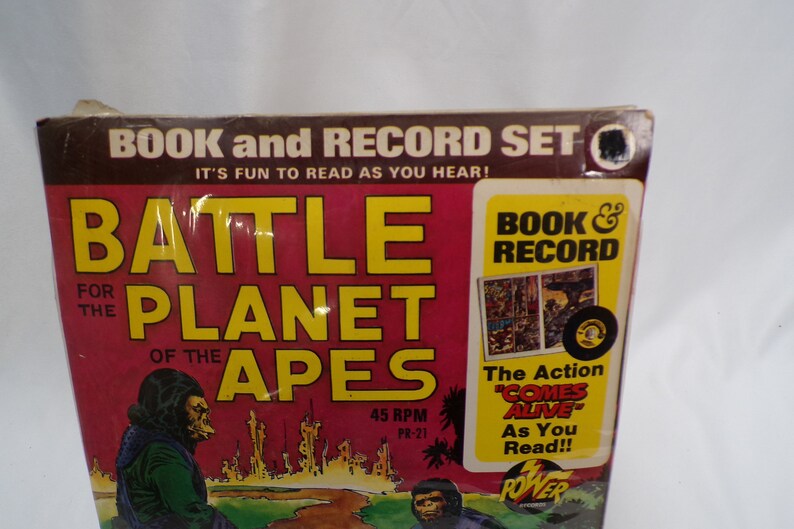 May include: A book and record set for "Battle for the Planet of the Apes". The cover features a red background with yellow text and a picture of a monkey in a green jacket. The record is black with a white label. The text on the cover reads "Book & Record" and "The Action "Comes Alive" As You Read!!"