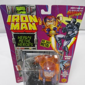 May include: An Iron Man action figure, featuring the character M.O.D.O.K. in a clear plastic case. The packaging is purple and features the Marvel Comics logo and the words "Heavy Metal Heroes". The figure is labeled "War Machine vs. M.O.D.O.K."