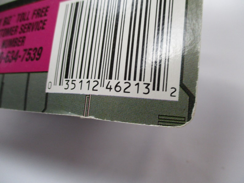 May include: Close-up of a product package corner with a barcode and the number "0 35112 46213 2". The package has a pink section with white text, including a toll-free customer service number.