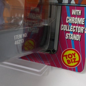 May include: Close-up of a toy package with the text "WITH CHROME COLLECTOR'S STAND!" and "TOY BIZ" logo. The item number is 46213. The packaging is pink, blue, and silver.