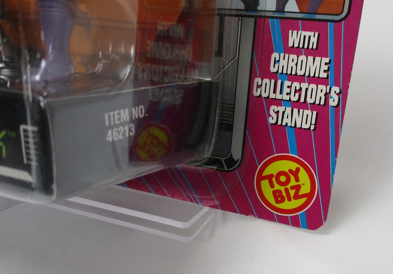 May include: Close-up of a toy package with the text "WITH CHROME COLLECTOR'S STAND!" and "TOY BIZ" logo. The item number is 46213. The packaging is pink, blue, and silver.