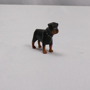 May include: Black and brown plastic toy Rottweiler dog figurine. The dog has a black collar with a silver buckle.