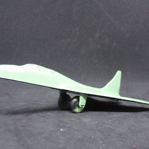 May include: A green toy airplane with a long, narrow wingspan and two black wheels. The airplane is made of metal and has a simple design.