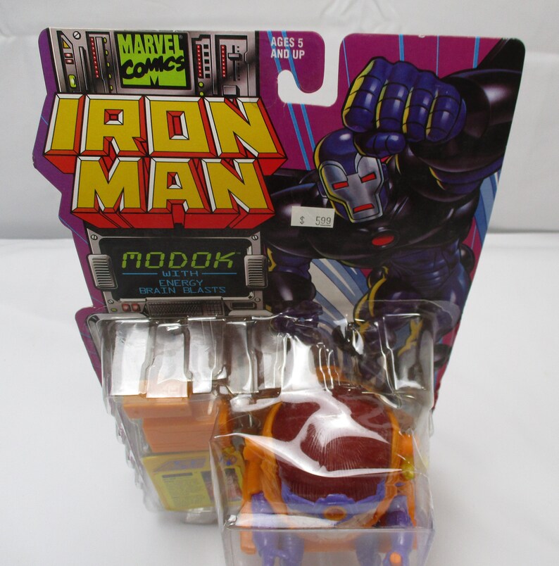 May include: A plastic action figure of MODOK, a Marvel Comics supervillain, with energy brain blasts. The figure is packaged in a clear plastic blister pack with a colorful cardboard backing featuring Iron Man and the text "MODOK with Energy Brain Blasts".