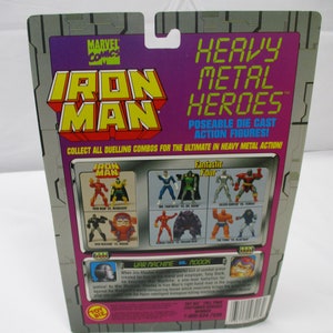 May include: A Marvel Comics Iron Man action figure package. The packaging features the Iron Man logo in yellow and red, with the words "Heavy Metal Heroes" in green. The back of the package shows various action figure combinations.