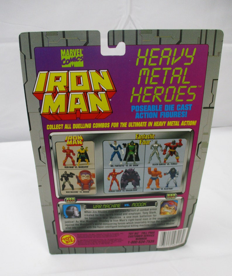 May include: A Marvel Comics Iron Man action figure package. The packaging features the Iron Man logo in yellow and red, with the words "Heavy Metal Heroes" in green. The back of the package shows various action figure combinations.