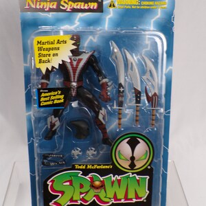 May include: A plastic package containing a Ninja Spawn action figure from Todd McFarlane's Spawn Deluxe Edition Ultra-Action Figures. The figure is black and red with green eyes and is holding a sword. The package is blue and green with the Spawn logo and the words "Ninja Spawn" and "Deluxe Edition".