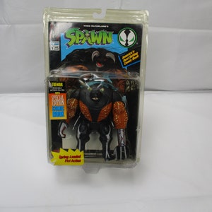May include: A packaged Spawn action figure featuring the character Tremor. The figure is black with orange accents and is labeled as a special edition with a comic book. The packaging includes the Spawn logo and the text "Spring-Loaded Fist Action."