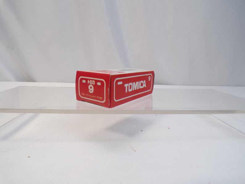 May include: A red Tomica box with white lettering and the number 9. The box is rectangular and sits on a clear surface. The Tomica logo is visible on the side of the box.