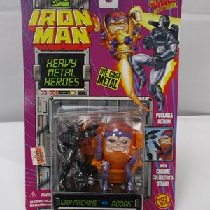 May include: Iron Man Heavy Metal Heroes action figure set featuring War Machine vs. MODOK. The packaging is purple and features comic book art. The set includes two poseable figures and a chrome collector's stand.