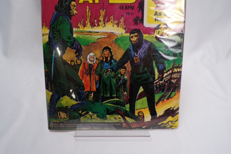 May include: A vintage comic book cover featuring a scene from the Planet of the Apes. The cover art depicts a group of apes in a jungle setting, with one ape holding a weapon. The text on the cover reads "Planet of the Apes" and "45 RPM YR-21".