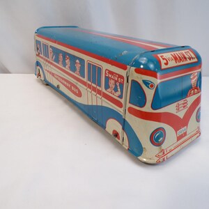 May include: Vintage toy bus in blue, red, and cream colors. The bus features the text "5 via Main St" and "Speedway Bus". The toy has illustrations of passengers and a driver. A classic collectible.