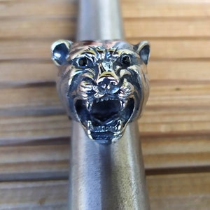 May include: A silver ring featuring a detailed, snarling panther head design. The panther's eyes are black gemstones.